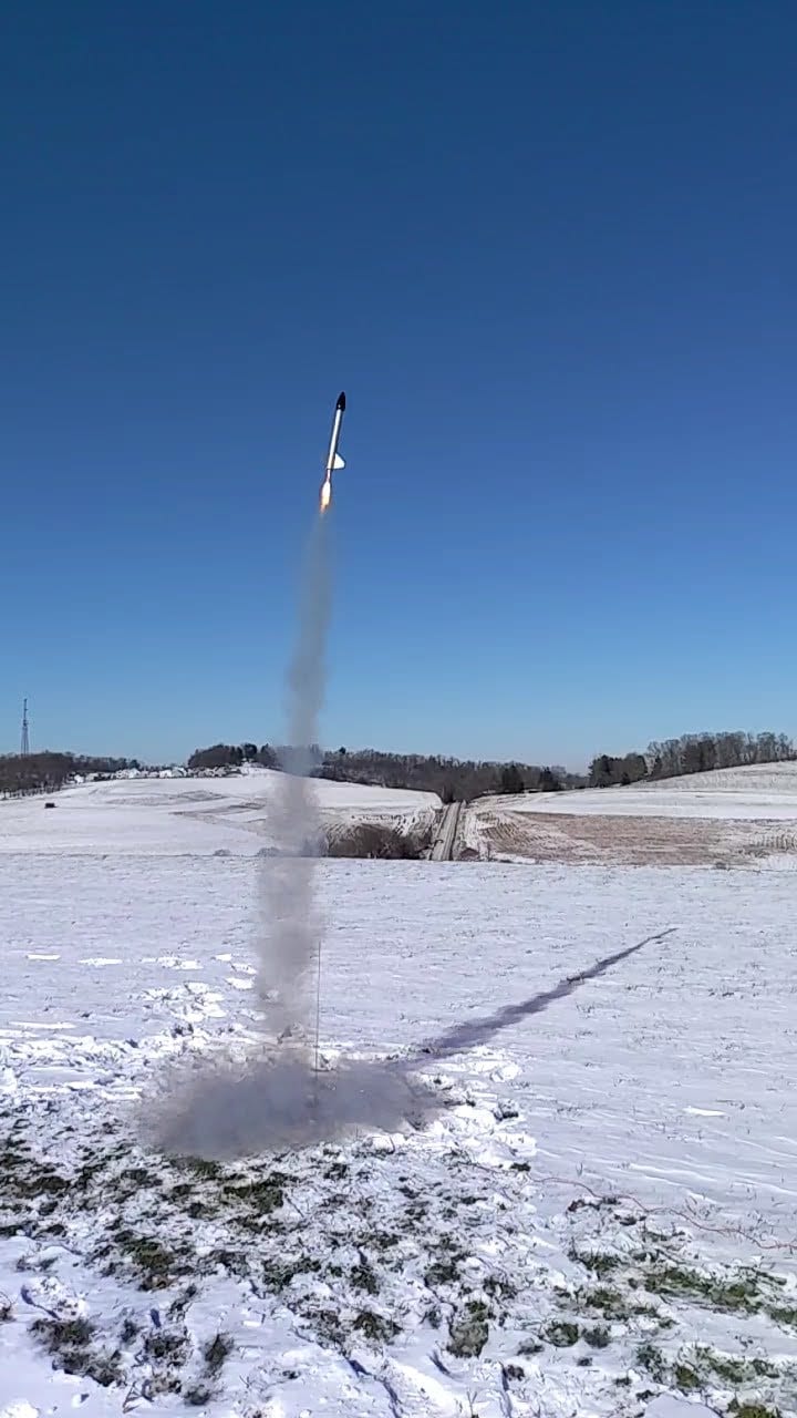The rocket lifting off from a snowy field with a long smoke trail